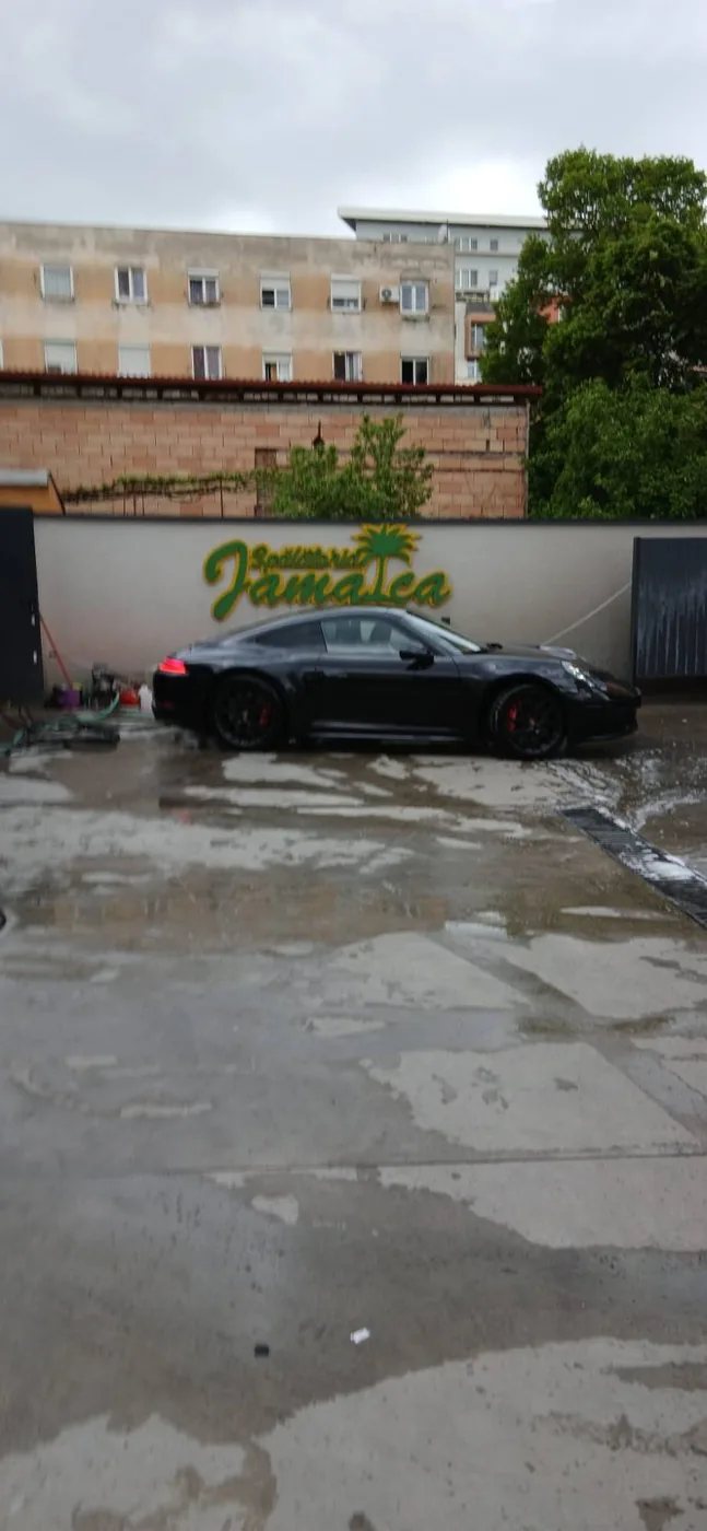 Porsche 911 negru parcat în fața peretelui cu sigla Jamaica