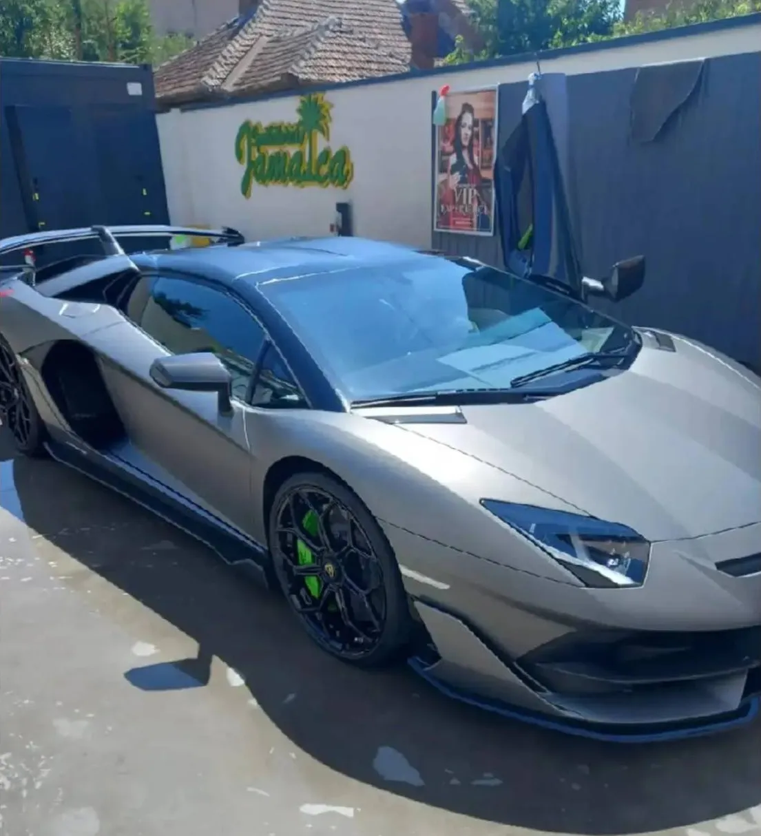 Lamborghini Aventador SVJ gri mat, cu etriere verzi, în fața siglei Spălătoriei Jamaica