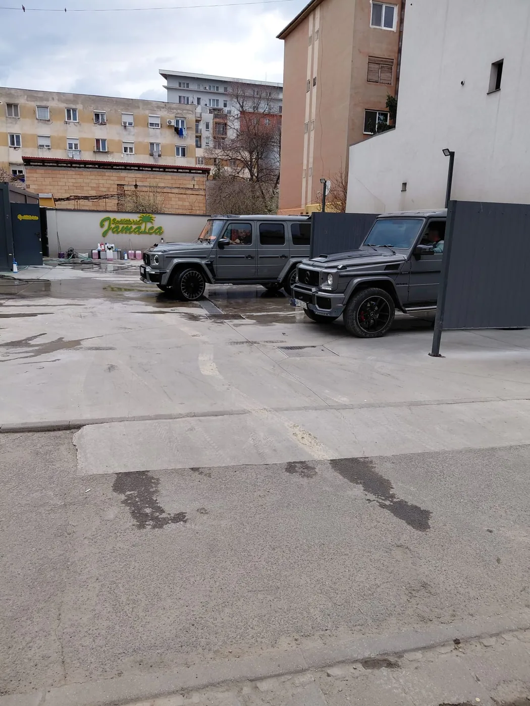 Două Mercedes-Benz Clasa G gri, unul lângă altul în fața siglei