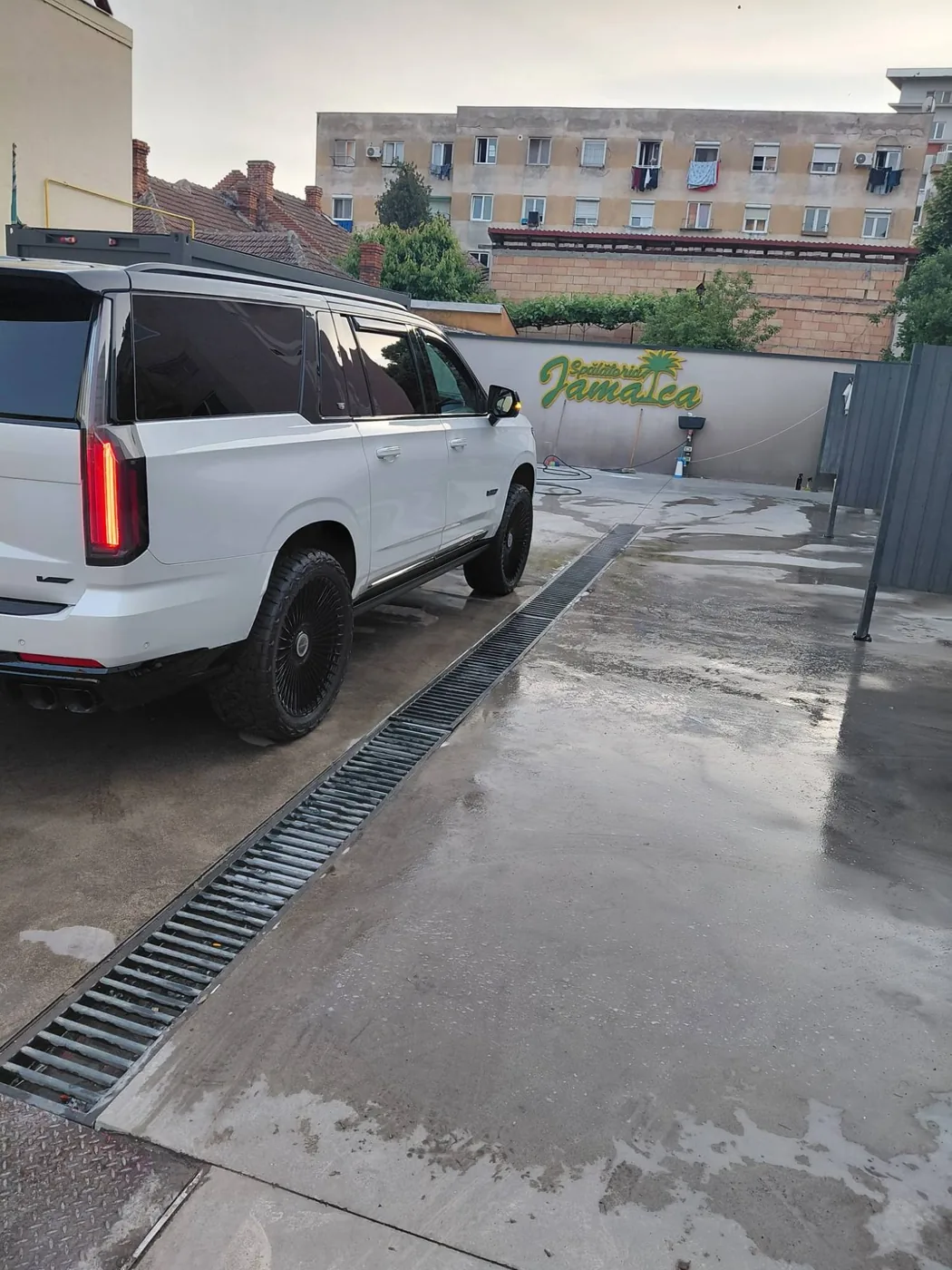 Cadillac Escalade alb pe jante negre, lângă rigola spălătoriei