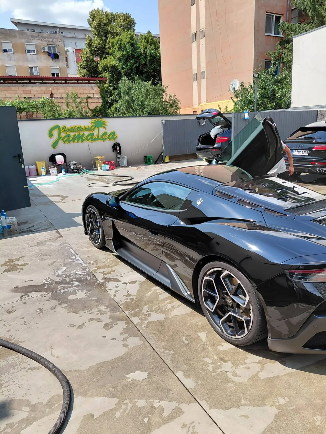 Maserati MC20 negru cu ușile ridicate, lângă sigla Spălătoriei Jamaica
