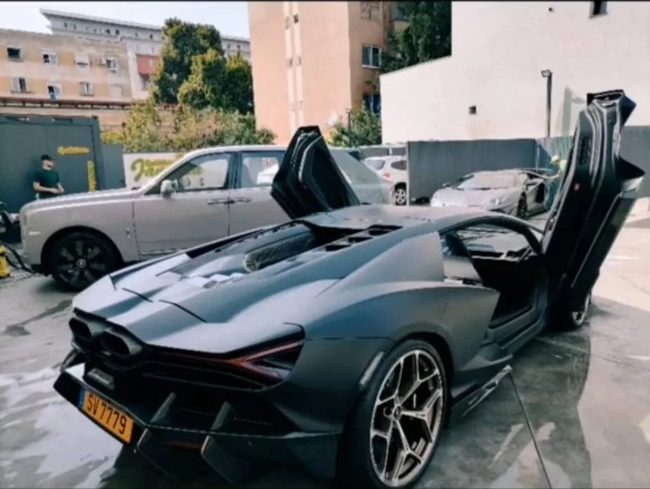 Lamborghini Revuelto gri mat cu ușile ridicate, lângă un Rolls-Royce, în curtea spălătoriei